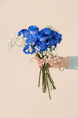 Hand with beautiful blue roses on color backgroundの写真素材
