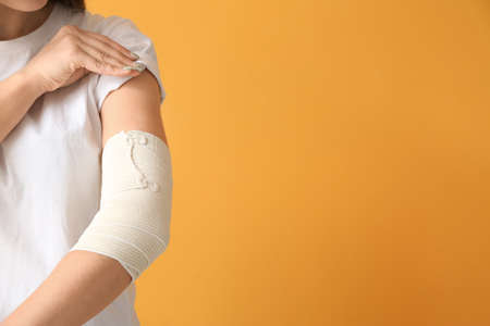 Young woman with bandaged arm on color backgroundの写真素材