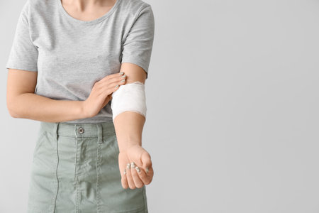 Young woman with bandaged arm on light backgroundの写真素材