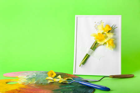 Creative composition with beautiful daffodils, paint palette and frame on color backgroundの写真素材