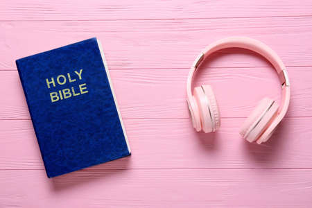 Holy Bible and modern headphones on color wooden background