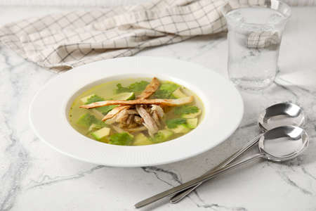 Plate with tasty Sopa de Lima soup and glass of water on light backgroundの写真素材