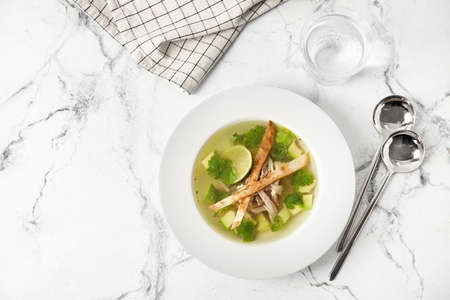 Plate with tasty Sopa de Lima soup and glass of water on light backgroundの写真素材
