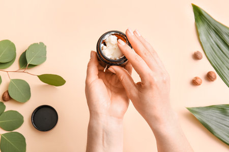Female hands with jar of shea butter, nuts and leaves on color backgroundの写真素材