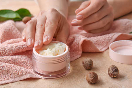 Female hands with jar of shea butter, nuts and towel on color background, closeupの写真素材
