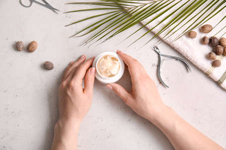 Female hands with jar of shea butter, nuts, tools for manicure and towel on light backgroundの写真素材
