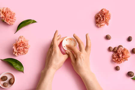 Female hands with jar of shea butter, nuts and flowers on color backgroundの写真素材