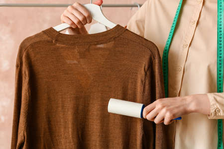 Woman cleaning jumper with lint roller on color backgroundの写真素材