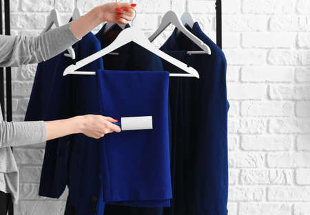 Woman cleaning clothes with lint roller on brick background