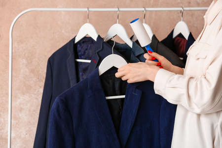 Woman cleaning jacket with lint roller on color backgroundの写真素材