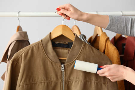 Woman cleaning bomber with lint roller on light backgroundの写真素材