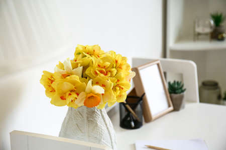 Bouquet of beautiful narcissus flowers on table near white wall