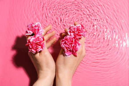 Female hands with flowers in water on color backgroundの写真素材