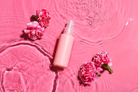 Bottle of cosmetic product and flowers in water on color backgroundの写真素材