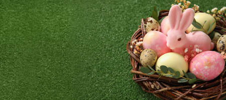 Nest with painted Easter eggs and bunny on green background with space for text