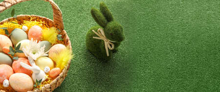 Basket of painted Easter eggs and bunny on green background with space for text