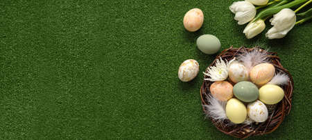 Nest with painted Easter eggs and tulips on green background with space for text
