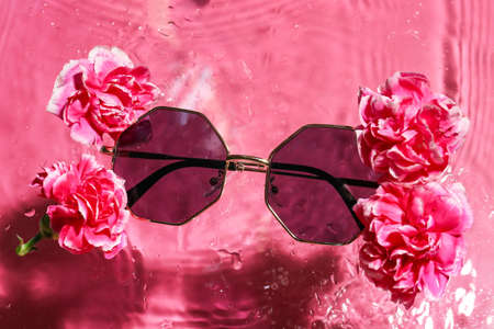 Stylish sunglasses and flowers on color background with water drops