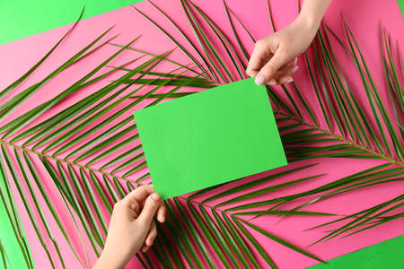Female hands with blank card and palm leaves on color backgroundの写真素材