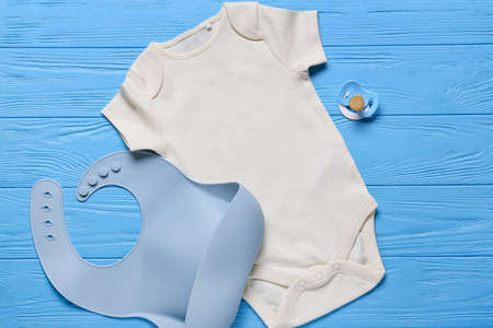 Baby clothes, bib and pacifier on color wooden backgroundの写真素材