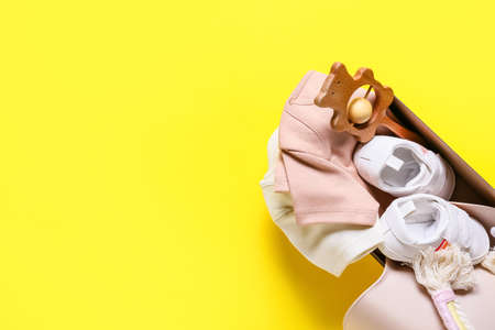 Box with baby clothes, shoes and toy on color background, closeup