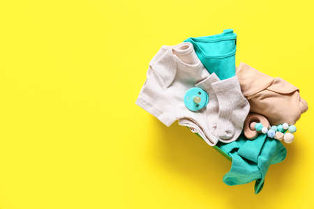 Box with baby clothes, teether and pacifier on color backgroundの写真素材