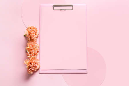 Clipboard with blank sheet of paper and flowers on color backgroundの写真素材