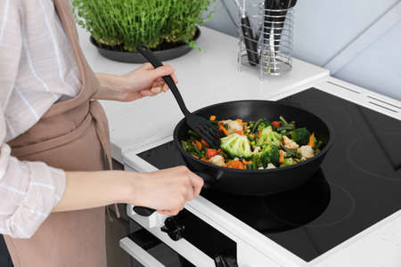woman frying vegetables on stove in kitchen