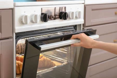 Woman opening oven with croissants in kitchenの写真素材
