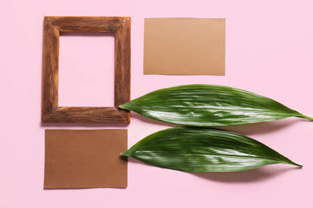 Composition with blank cards, empty picture frame and green leaves on color background