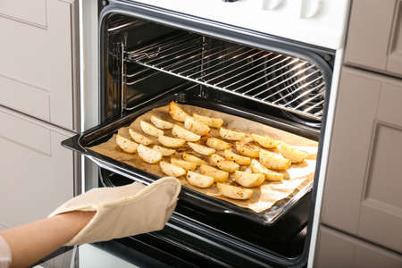 Woman taking baking tray with fresh potato out of ovenの写真素材