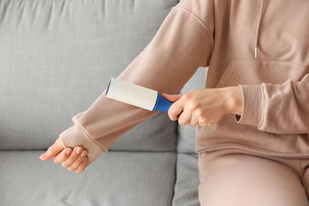 Woman cleaning clothes with lint roller, closeup