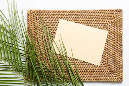 Composition with blank card, wicker mat and palm leaves on white background