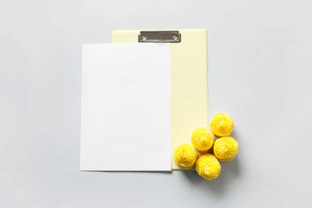 Composition with blank sheet of paper, clipboard and tasty cupcakes on gray background