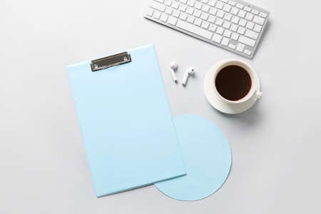 Composition with clipboard, earphones, keyboard and cup of coffee on light background