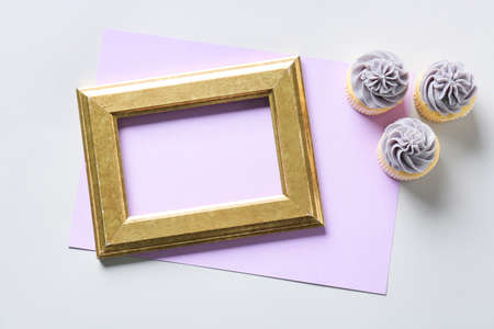 Composition with blank sheet of paper, empty picture frame and tasty cupcakes on light background