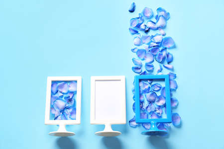 Empty picture frames and rose petals on color background