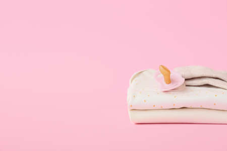 Stack of baby clothes and pacifier on color backgroundの写真素材