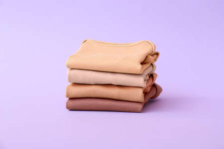 Stack of baby clothes on color background