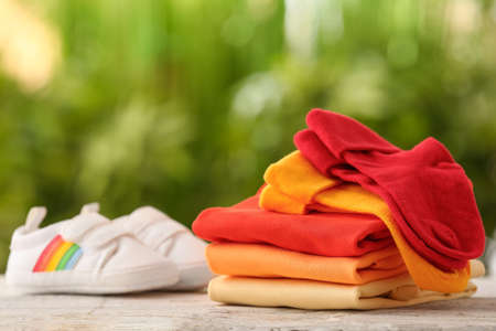 Stack of baby clothes and shoes on wooden table outdoorsの写真素材