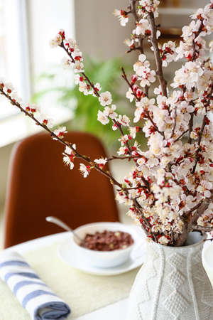 Vase with beautiful blossoming branches on dining table in kitchen