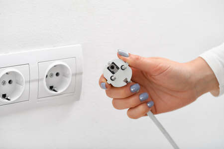 Woman putting plug into socket in roomの写真素材