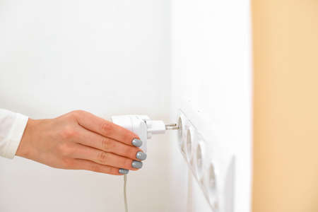 Woman putting plug into socket in room, closeup