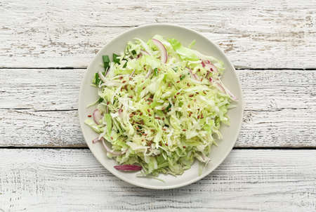 Plate with tasty cabbage salad on light wooden tableの写真素材