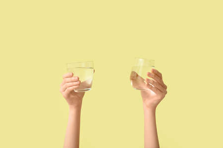 Female hands with glasses of water on color backgroundの写真素材