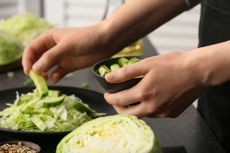 Female chef cooking tasty cabbage salad on table in kitchen, closeupの写真素材