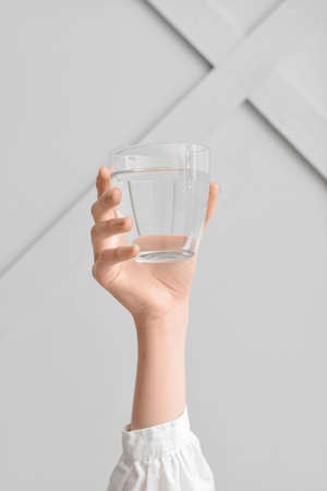 Female hand with glass of water on light background