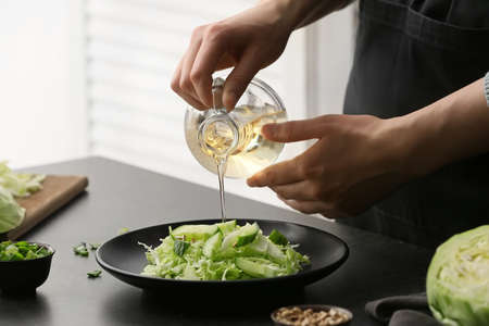 Female chef cooking tasty cabbage salad on table in kitchen, closeupの写真素材