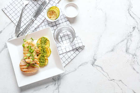 Plate with tasty grilled chicken meat, zucchini and pesto sauce on light backgroundの写真素材