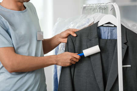 Male worker cleaning clothes with lint roller at modern dry-cleaner'sの写真素材